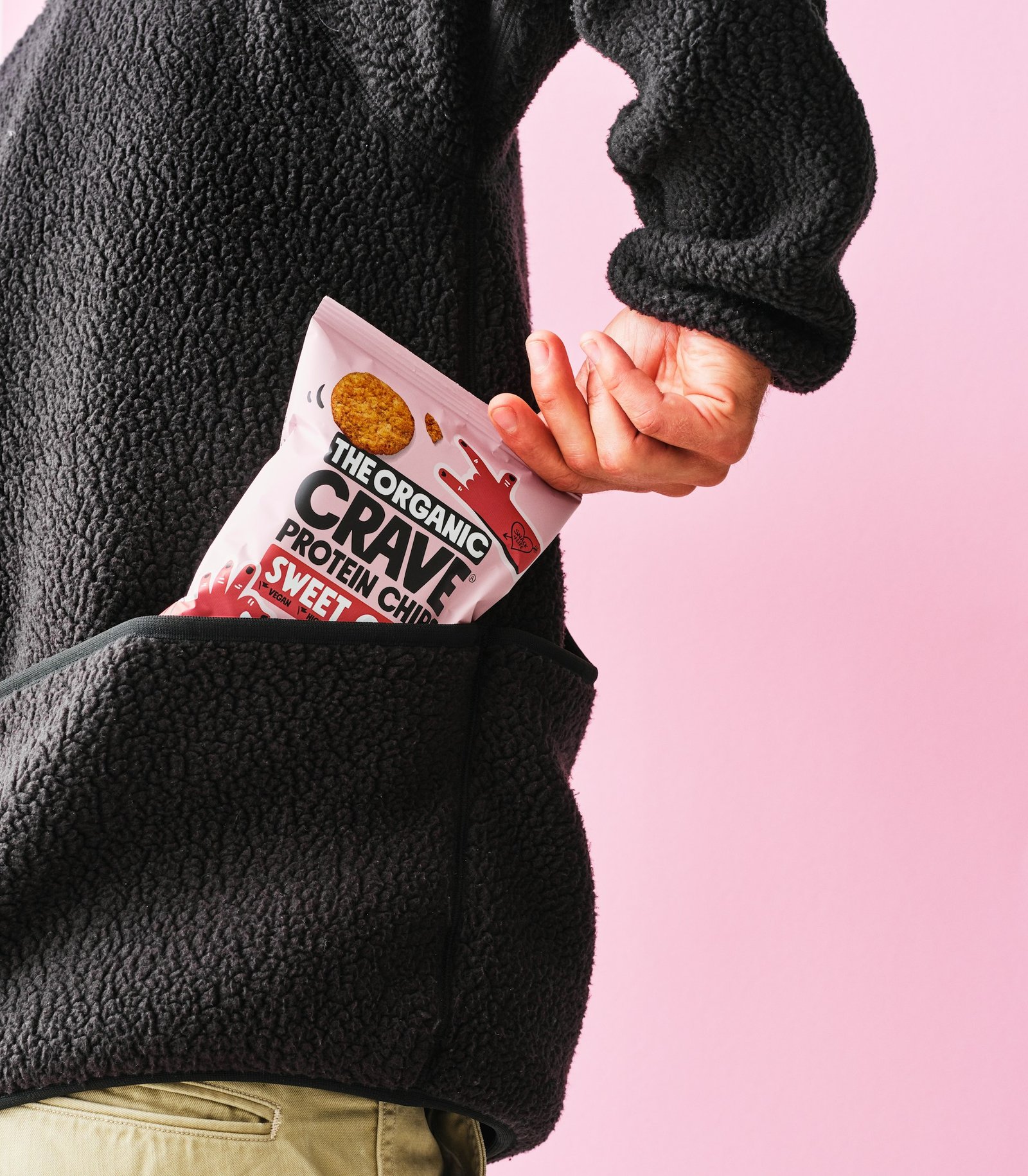 A hand pulling a bag of protein chips from a fleece jacket pocket